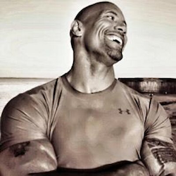 The Rock, wearing a fitted t-shirt, laughing.