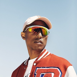 Pharrell Williams wearing speed dealer sunglasses and a cap, standing in the sun.